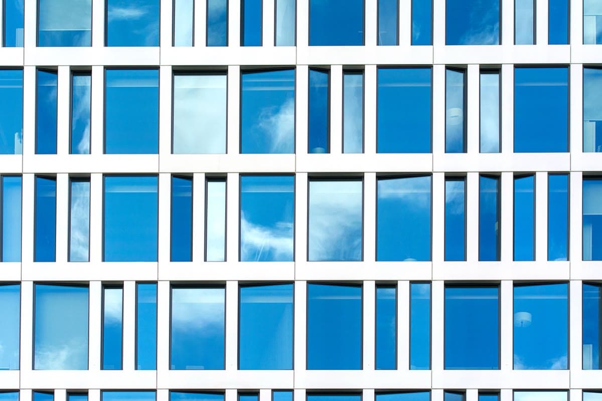 Blue glass curtain wall with clean facade grid — a thermal break isolator profile sits hidden inside every joint of the mullion and transom framing
