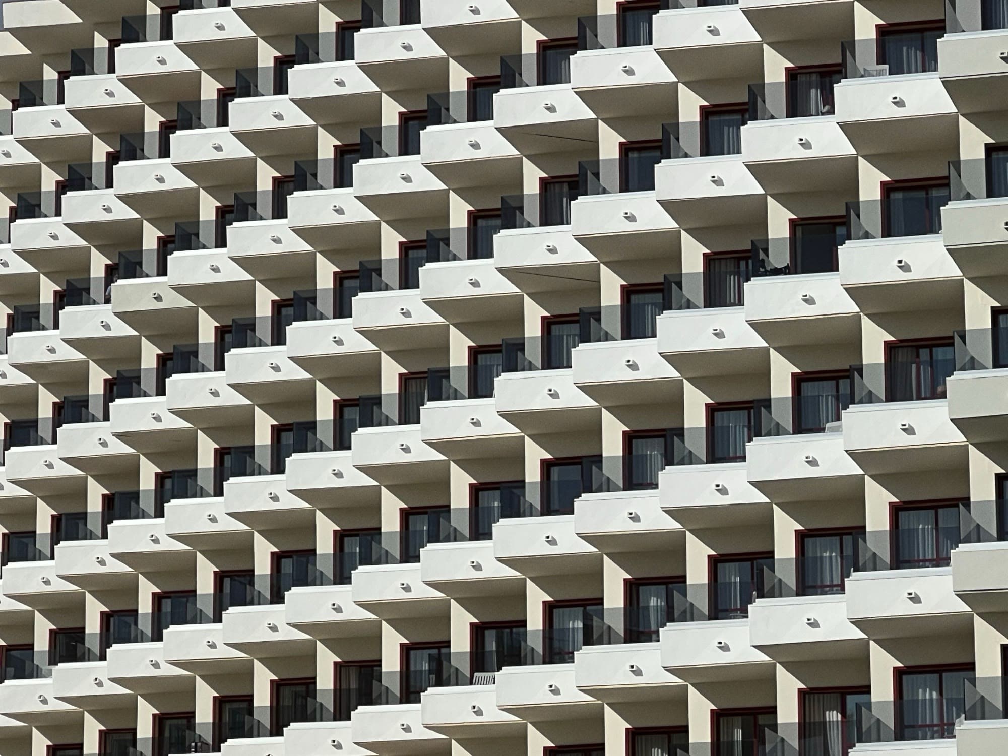 Residential facade grid of hundreds of identical aluminum-framed windows and balconies — every one of those frames depends on a pair of thermal break profiles to meet its energy code