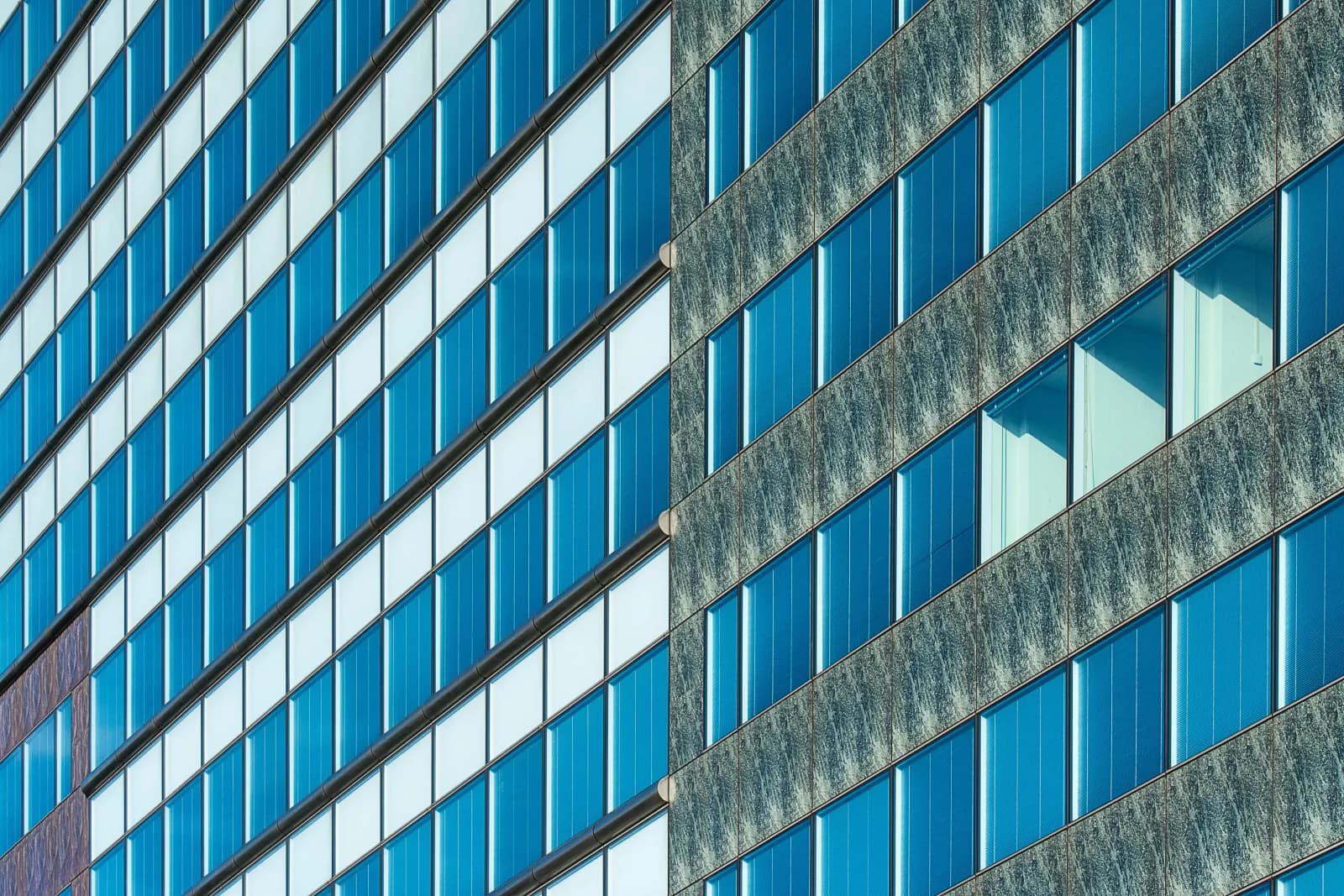 Blue glass curtain wall facade grid of mullions and transoms — the primary structural frame this article addresses, not the hidden thermal break inside it