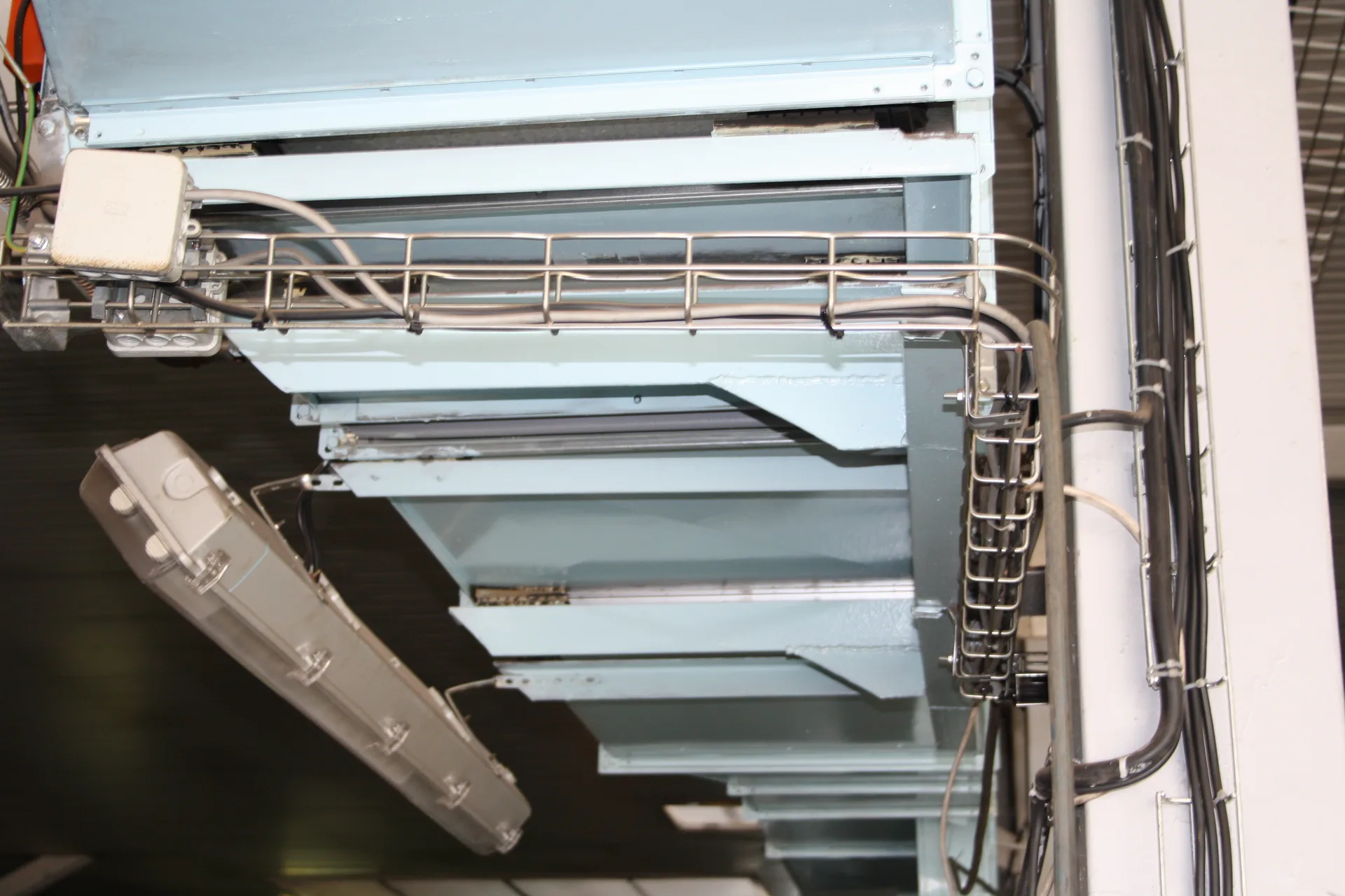 Metal wire-mesh cable tray carrying cables around a corner beneath a steel stair structure