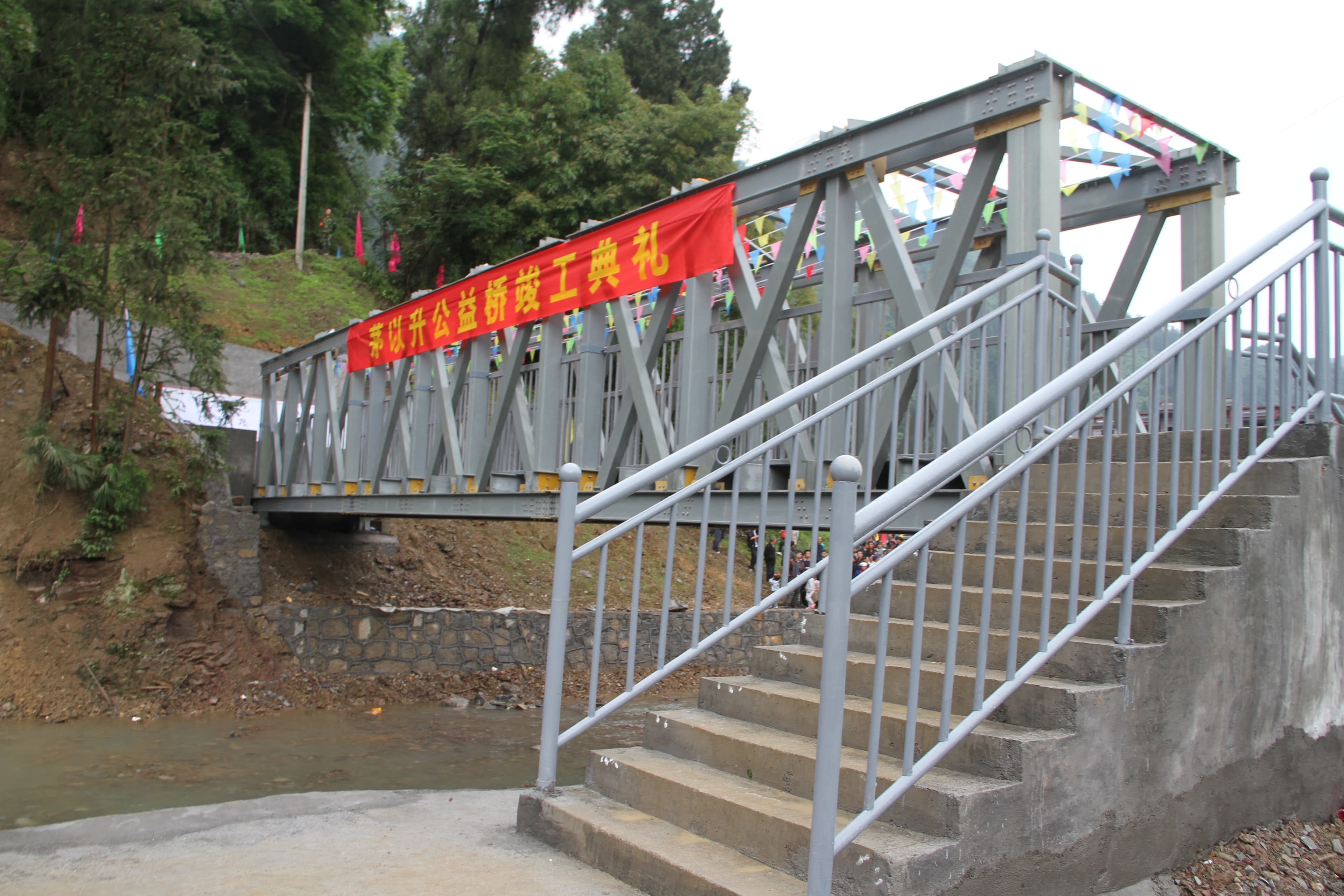 The Mao Yisheng Charity Bridge in Pengshui at its completion ceremony, with the truss spanning the river and stepped approaches; photograph published by the Mao Yisheng Foundation