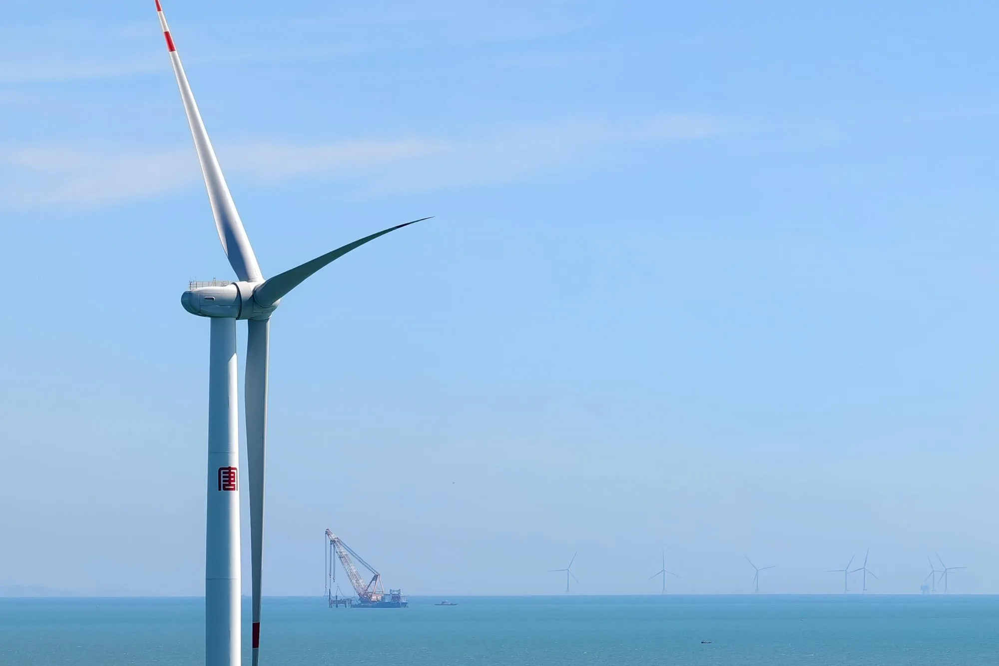 Offshore wind turbine with crew transfer vessel showing the structural scale that drives CFRP-spar-cap selection in long blades