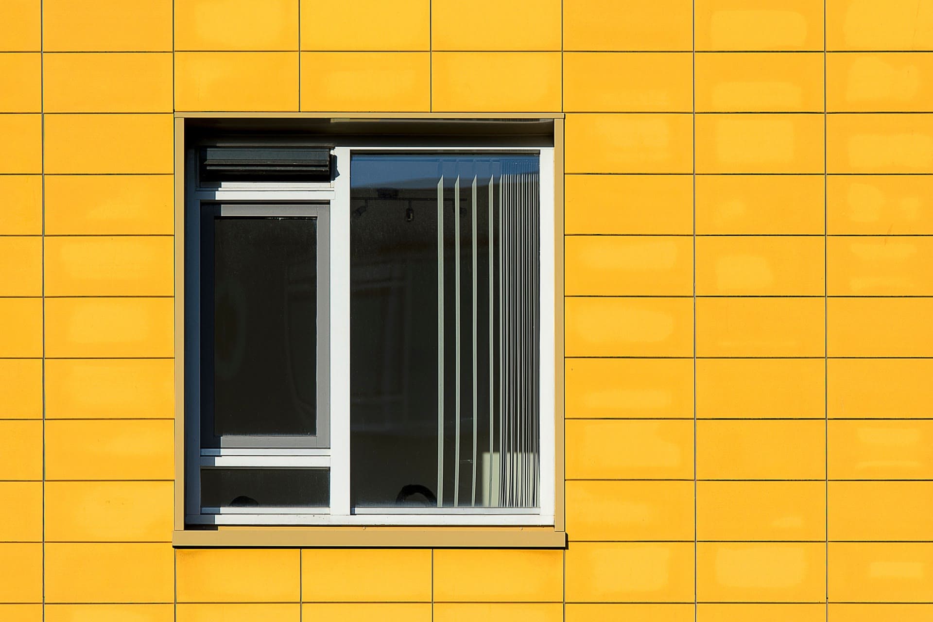 Modern window set in a bright yellow tiled facade — what a window profile costs is decided long before it reaches the wall