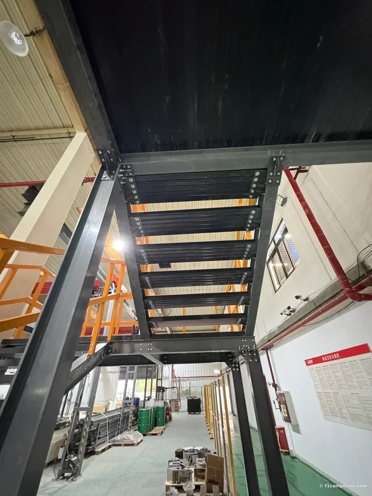 Underside of the stair flight: FRP I-beam stringers carrying the treads, with the orange FRP handrail alongside