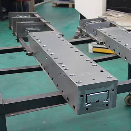 Long steel channel-profile die with a series of guide plates mounted behind it on the tooling frame
