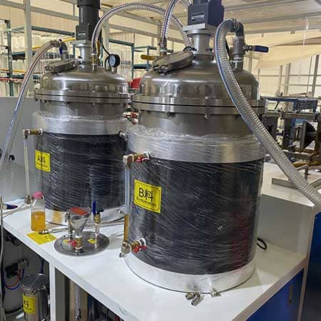 Two stainless-steel resin component tanks with agitator motors and flexible hoses in the supplier workshop