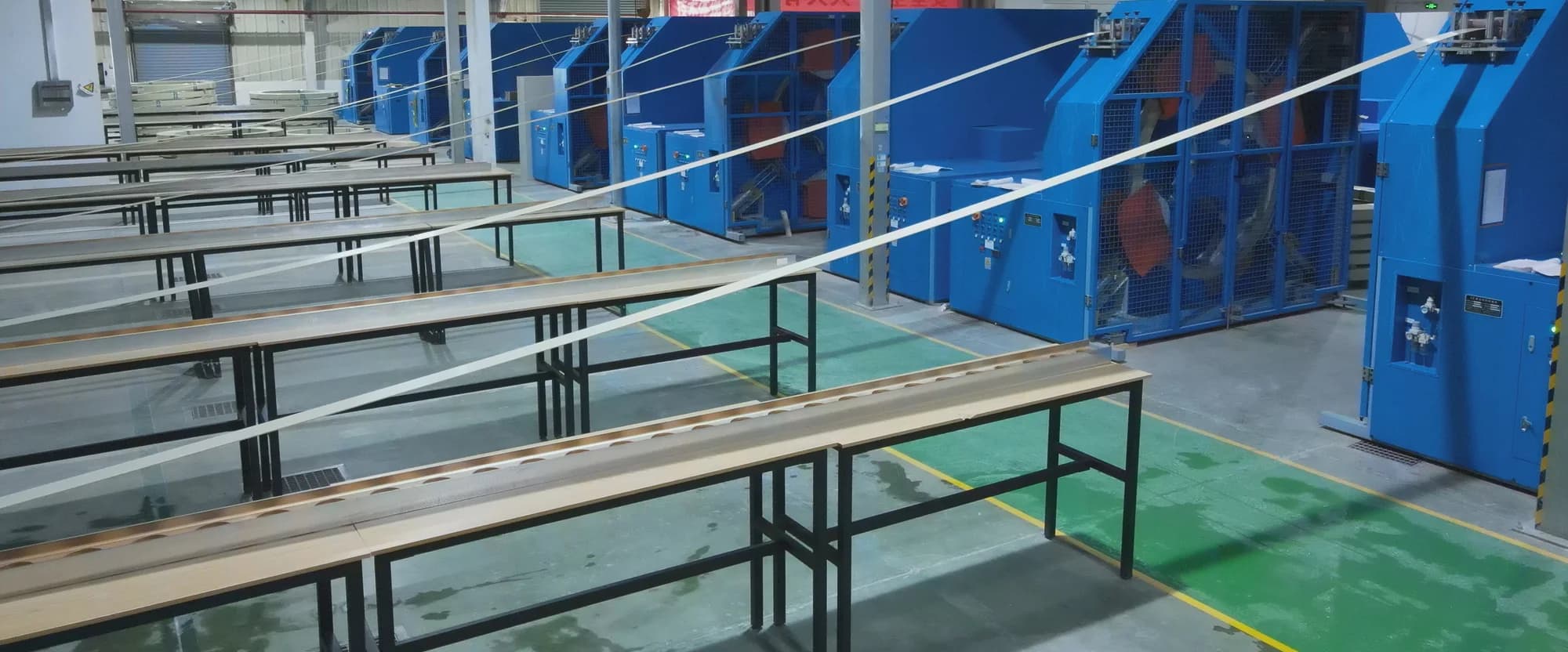 F1 Composite pultrusion plant floor — finished pultruded profiles on inspection tables alongside fiber-handling and pulling equipment